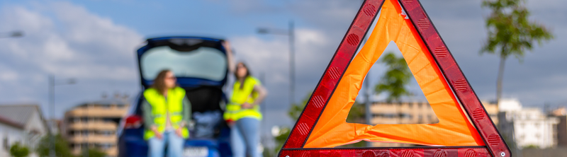 Warning triangle in foreground with roadside emergency responders at an open car trunk