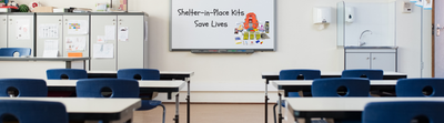 Classroom whiteboard reading "Shelter-in-Place Kits Save Lives" next to the Safety Kits Plus Shelter-in-Place Preparedness backpack and its contents.